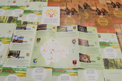 Opis. Na zdjęciu ulotki pt."... z historią w tle" i "Przygoda na okrągło" prezentujące walory powiatu szczycieńskiego oraz logo Południowe Mazury.